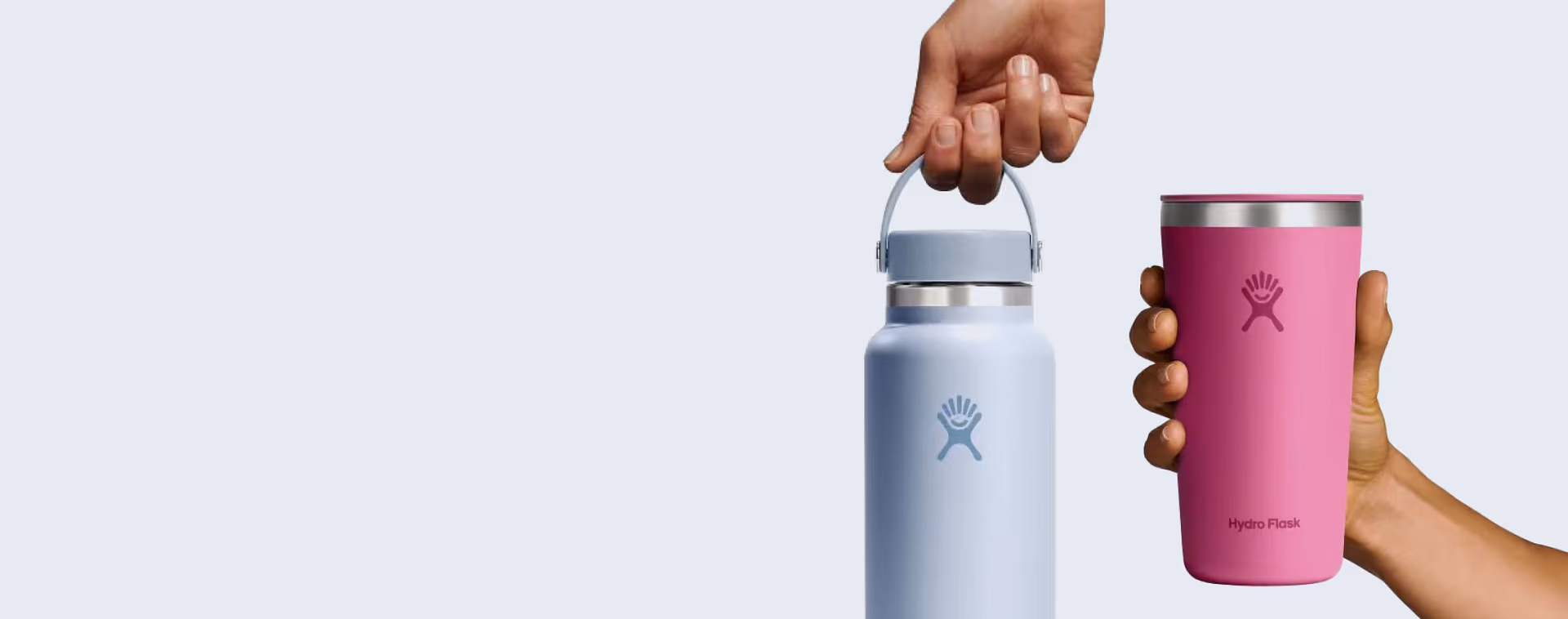 Hand holding a Hydro Flask water bottle and another hand holding a pink Hydro Flask tumbler.
