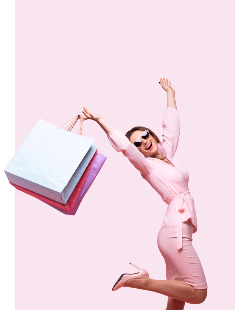 Happy woman in pink dress and heels jumping with shopping bags against a pink background.